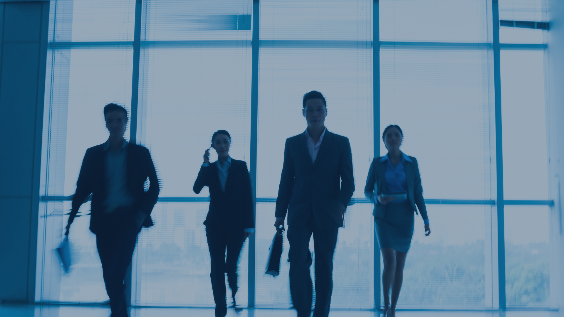 Fünf Business-Personen gehen entschlossen durch ein modernes Bürogebäude mit Glasfassade